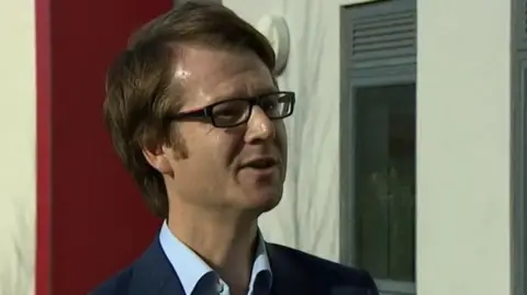 Toby Sanders with medium-length brown hair and glasses