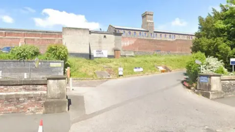 Google One of the high walls with a sign saying 'HMP Lewes' on it