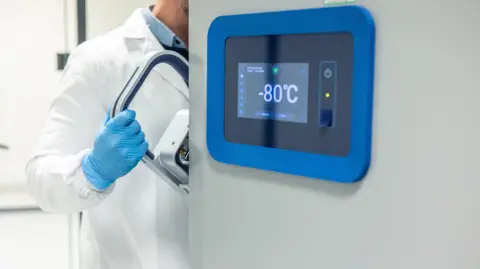 Getty Images Scientist in a white lab coat and gloves opening an ultra-low temperature freezer in a scientific laboratory, which says -80°C in a panel on the door.