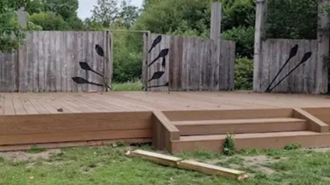 An open theatre with damaged wooden fencing and platform. 