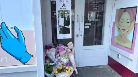 Flowers left in the doorway of a beauty salon. A picture of Abdhi Patel is on the door.