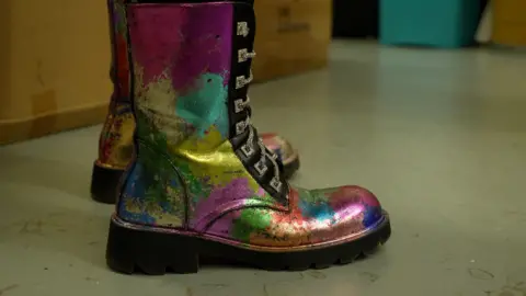 A pair of lace-up boots spray-painted in bright multi-colours: pink, yellow, blue and green.