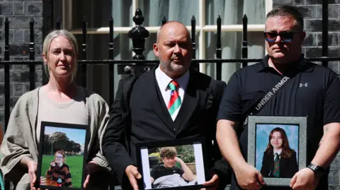 Stuart Stephens is joined by two other parents outside Downing Street holding up images of their deceased children.