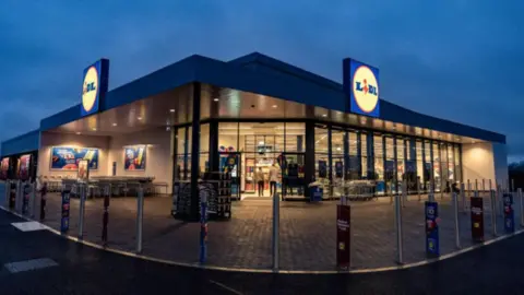 Lidl store. There is a concrete pavement. It is a supermarket with the big blue and yellow Lidl sign.