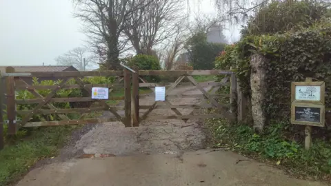 The wooden gates of Orchard Organic Farm are closed and have official notices posted to them.  