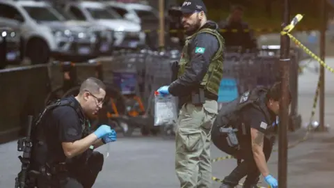 Getty Images A Brazilian police officer kneeling down on the left of the picture takes samples at São Paulo airport. Another officer stands holding a see-through bag, while another officer on the right bends down to pick something up. 