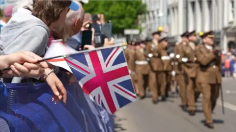 A picture of people holding flags as they watch the parade go past. 