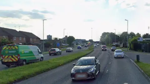 A google streetview image of the road, showing cars driving along it