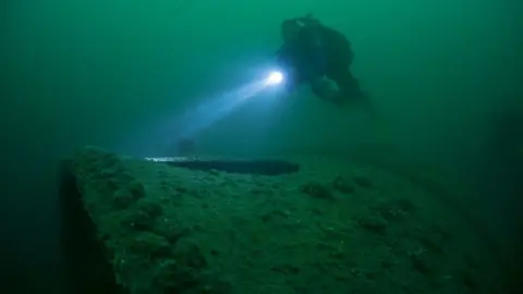Martin Davies A diver can be seen deep in the water, shining a beam of torchlight onto part of the wreckage of the sunken SS Mendi. 