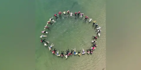 Tyne and Wear Fire and Rescue Service An overhead shot of a large group of people in a circle in the sea