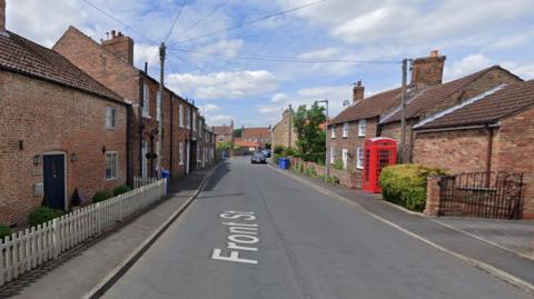 A view of Front Street in Laxton in East Yorkshire, with red brick cottages either side of the road and a red phone box on the right hand side of the road