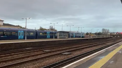 Empty train lines at Paddock Wood station, as seen from the platform. In the background there's a blue Southeastern train on a different platform.