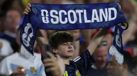 Getty A boy among the crowd at the World Cup holding up a Scotland scarf. There are people in the crowd behind him.
