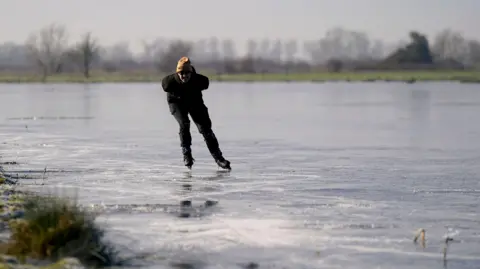 PA Media Ugo Sassi from Cambridge skates on a frozen flooded field in Upware, Cambridgeshire.