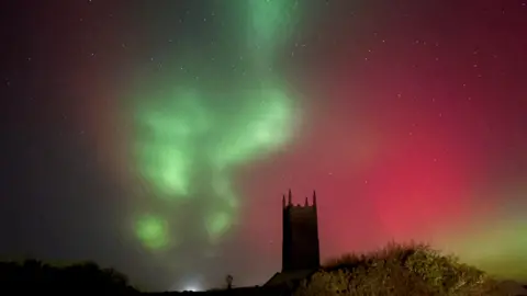 A green and pink sky studded with stars shines above a church tower.