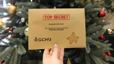 GCHQ A woman's manicured hand holding an envelope in front of a Chrsitmas tree