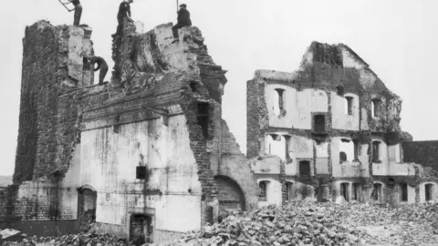 Getty Images A black and white image of a demolition site of workers breaking down the old prison site. Lots of rubble and walls left.