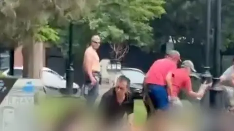 People helping others on the ground in Colorado park with suspect standing nearby watching