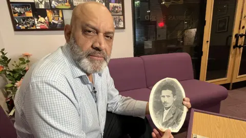 Kash Kumar holding up a black and white portrait of his grandfather