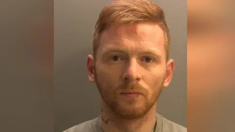 Cumbria police A mugshot of Jack Slaven. He has short ginger hair, blue eyes and a beard. He is wearing a grey jumper and had a neck tattoo.