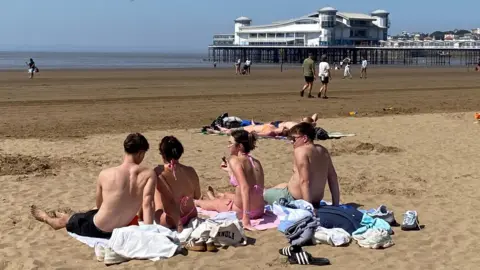A group of four young people with their backs to the camera sunbathe on the beach at Weston-super-Mare in Somerset