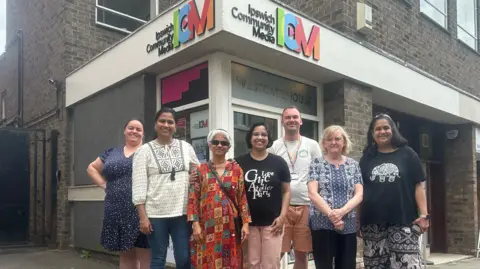ICM Seven people stand in front of a building. There is colour branding on the doorway which reads Ipswich Community media