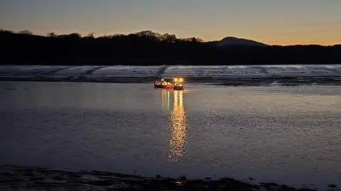 A rescue boat heads out to water in the dark with its lights beaming out