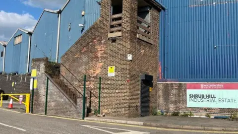 An industrial building, with blue corrugated sheeting and brick-built sections. There is a sign with the words Shrub Hill Industrial Estate in capital lettering.