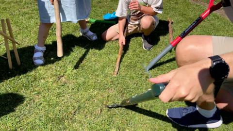 A picture shows a man and two children hitting the ground with spades and sticks as part of the World Worm Charming Championships. 