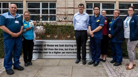 Staff standing in front of the steel memorial, which has butterflies and a quote