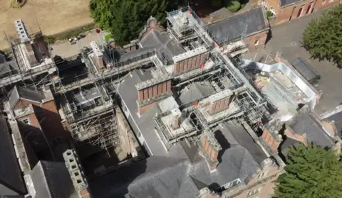 BBC An drone-taken aerial view of scaffolding on top of a large red brick building 