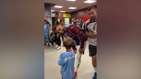 Alan Kearney Image shows Mo Salah leaning down to talk to little Isaac Kearney. They are in the dressing room at the club, and are both wearing the club's kit. 