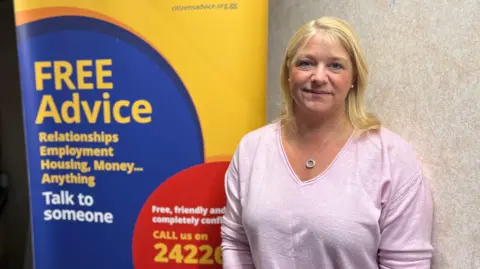 BBC Ali Marquis stood in front of a Citizens Advice Guernsey poster