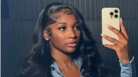 Ashly Robinson in a blue top, holding a phone as she takes a selfie of herself