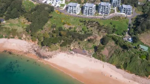 An aerial view of the beach and the cafe at Portelet Bay, with houses seen on the hill behind.