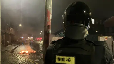 Riot police officer on Blythe Street with small fire in background