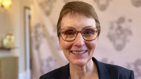 A recent photo of Helen Sharman smiling at the camera. She has short brown hair and is wearing rimmed glasses