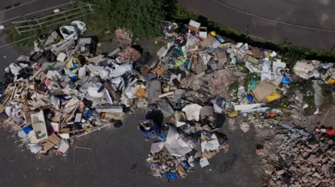 Glastonbury Gabriel Drone shot from the air of loads of rubbish and rubble on an old car park. There's wood, a bath tub, soil, blankets, old beds and much more. 