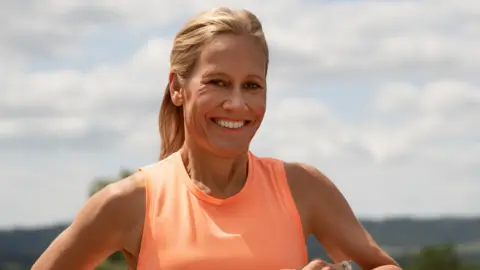 Sophie Raworth smiling at the camera. She is wearing a neon orange tank top. 