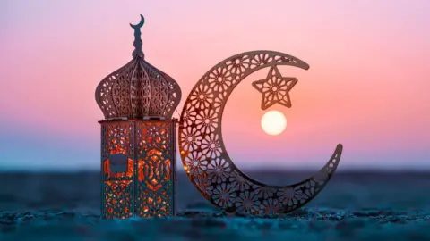 Lantern and crescent moon on the beach at sunset.