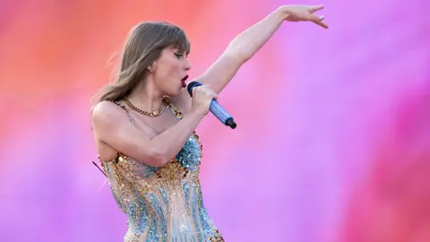 PA Media Taylor Swift performing in a sparkling white and blue outfit and holding a blue microphone