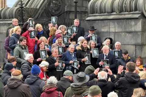Michael Sturrock A large crowd of people standing on steps outside the church holding pictures of Jane.