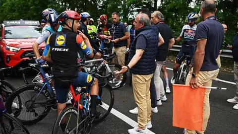 Riders in stage six of the Giro d'Italia wait on their bikes after being delayed following a crash