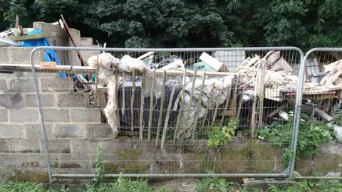 Environment Agency A metal fence in front of a pile of rubbish including windows and wood