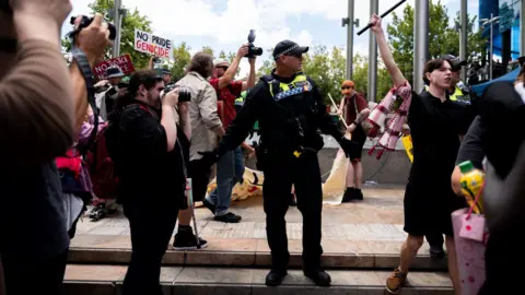 A police officer looks on as protesters wave flags and signs - one saying 'no pride genocide' and a Palestinian flag in view - in Perth on Monday.