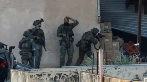 Israeli troops in Jenin take position behind a wall in front of a garage door before Palestinians emerge from it, in Jenin on Thursday