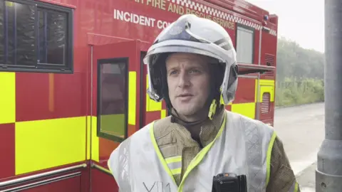 Group manager Dale Howey in his firefighter uniform standing in front of an incident command vehicle