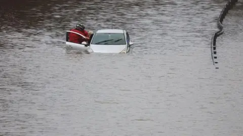 Reuters Firefighters rescue a man from his car, it is submerged up to its bonnet in floodwater.