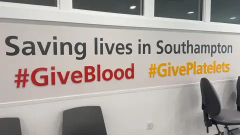 Image shows a wall which says 'Saving lives in Southampton" written in grey. Underneath, it says hashtag "Give Blood" in red and hashtag "Give Platelets" in yellow. 