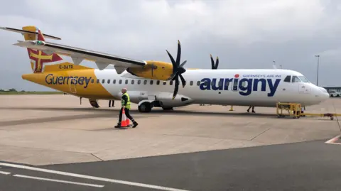 BBC A white and yellow plane with the word Aurigny on the side. Propellors on each wing. 